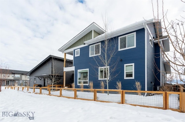 snow covered property with fence and board and batten siding