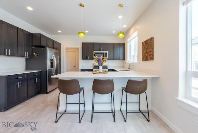 kitchen with a peninsula, appliances with stainless steel finishes, a breakfast bar, and a sink