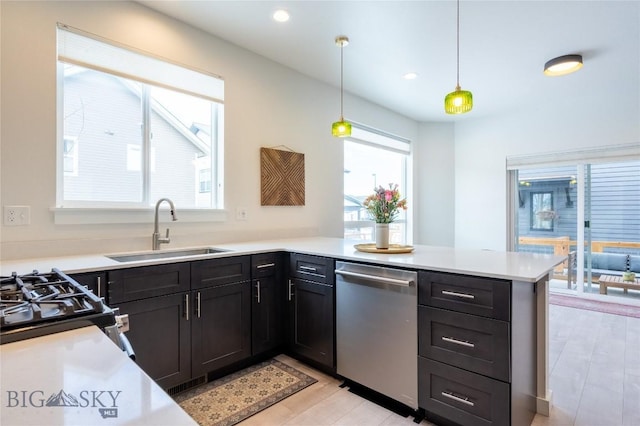 kitchen featuring dishwasher, decorative light fixtures, a peninsula, light countertops, and a sink