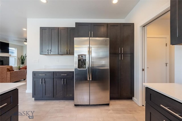 kitchen with light countertops, stainless steel fridge, a tiled fireplace, and recessed lighting