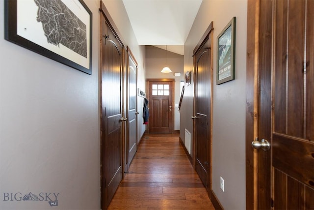 corridor with a barn door, visible vents, dark wood finished floors, baseboards, and vaulted ceiling