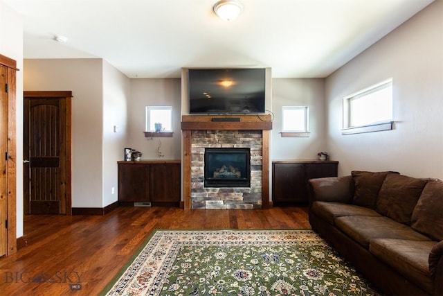 living room featuring a healthy amount of sunlight, a stone fireplace, baseboards, and wood finished floors