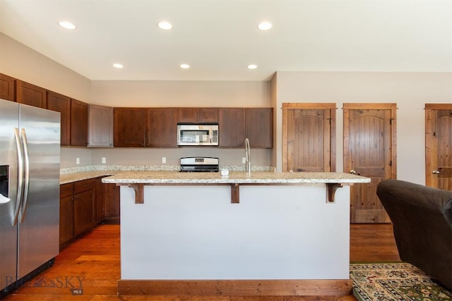 kitchen with appliances with stainless steel finishes, a breakfast bar area, and wood finished floors