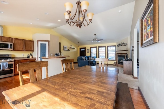 dining space with baseboards, lofted ceiling, ceiling fan, wood finished floors, and a fireplace