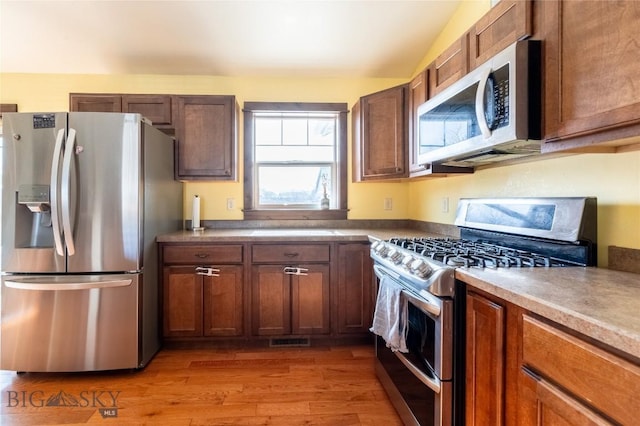 kitchen with stainless steel appliances, lofted ceiling, visible vents, light wood-style flooring, and brown cabinetry