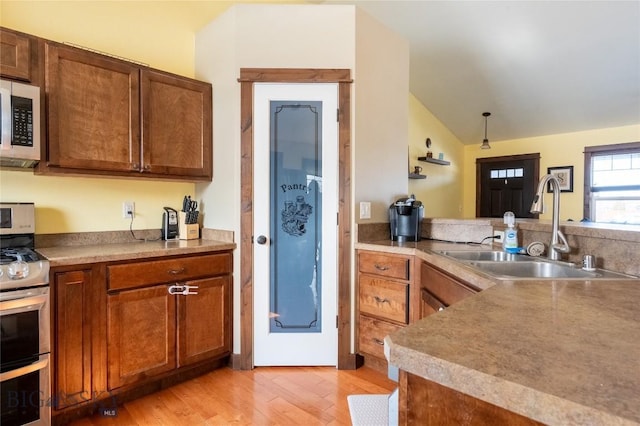 kitchen with light wood-style flooring, brown cabinets, vaulted ceiling, stainless steel appliances, and a sink