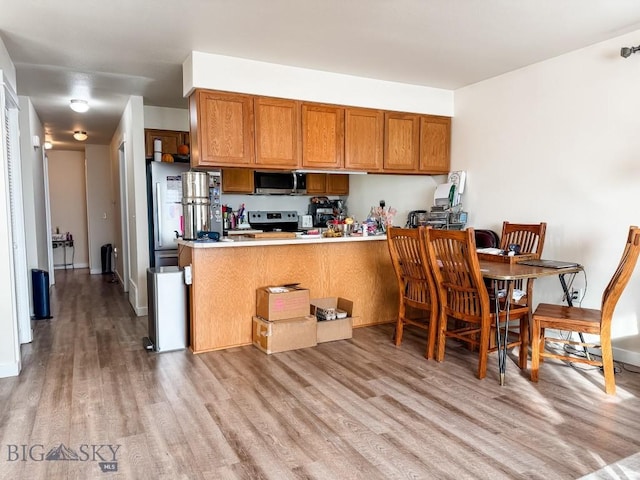 kitchen with light wood-style flooring, stainless steel appliances, a peninsula, light countertops, and brown cabinets