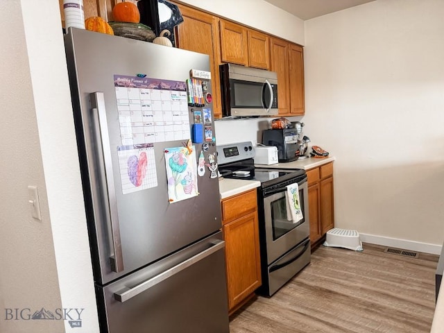 kitchen featuring light countertops, visible vents, appliances with stainless steel finishes, brown cabinetry, and light wood-style floors