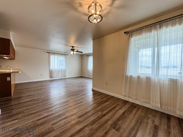 unfurnished living room featuring baseboards, dark wood-style floors, a sink, and ceiling fan with notable chandelier