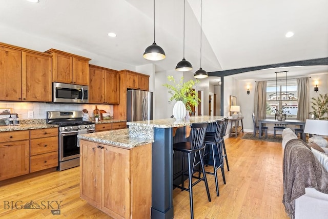 kitchen featuring light wood finished floors, stainless steel appliances, brown cabinetry, vaulted ceiling, and a kitchen island