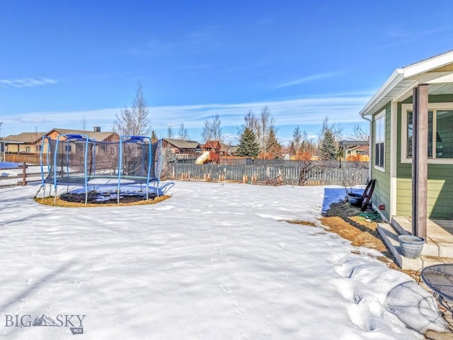 snowy yard featuring a trampoline and fence