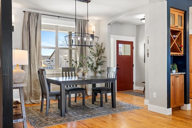 dining room with light wood-style floors, arched walkways, a chandelier, and baseboards