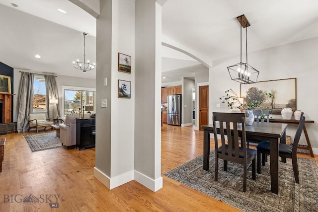 dining area featuring light wood-style floors, a fireplace with raised hearth, baseboards, and an inviting chandelier