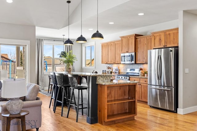 kitchen featuring decorative backsplash, light wood-style flooring, a breakfast bar area, light stone countertops, and stainless steel appliances