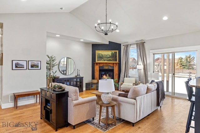 living room featuring light wood finished floors, recessed lighting, a notable chandelier, and a glass covered fireplace