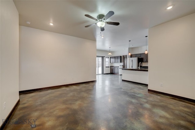 unfurnished living room featuring concrete floors, baseboards, and a sink