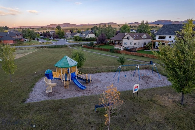 playground at dusk featuring a lawn, a mountain view, and playground community