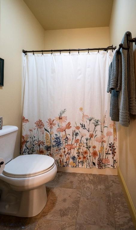 bathroom featuring toilet, curtained shower, and baseboards