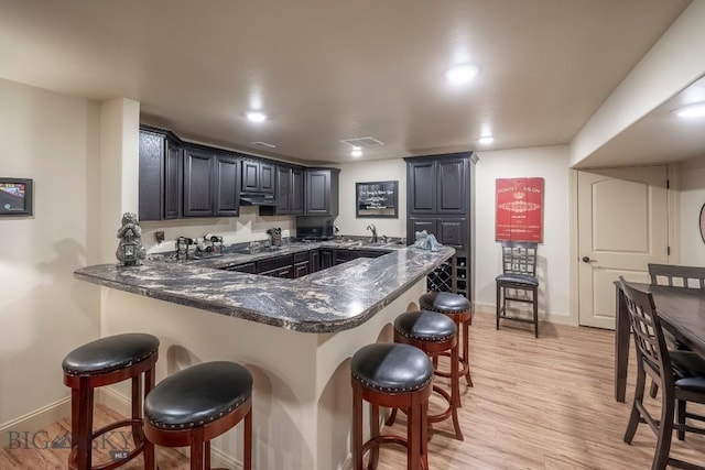 kitchen with a breakfast bar area, visible vents, light wood-style flooring, a peninsula, and baseboards