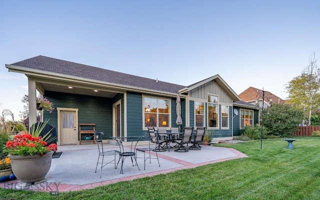 rear view of house with a patio, a lawn, board and batten siding, and fence