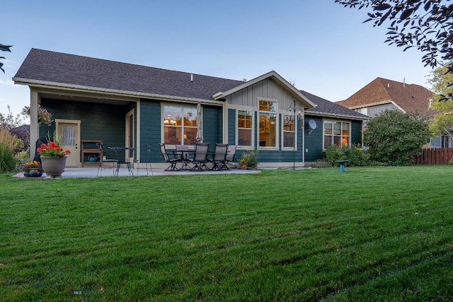 rear view of house with board and batten siding, a patio area, a lawn, and fence