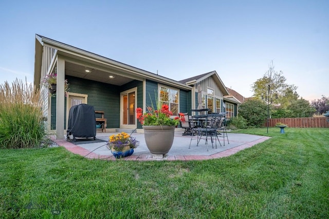 rear view of property featuring board and batten siding, a patio area, fence, and a lawn