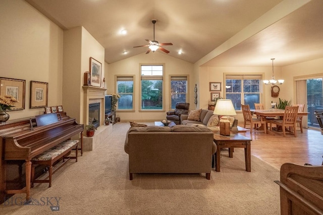 living room with light wood-type flooring, a glass covered fireplace, high vaulted ceiling, and ceiling fan with notable chandelier