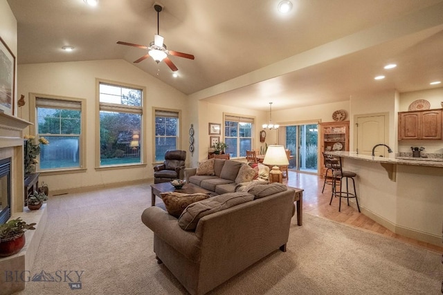 living area with lofted ceiling, recessed lighting, ceiling fan with notable chandelier, baseboards, and a glass covered fireplace