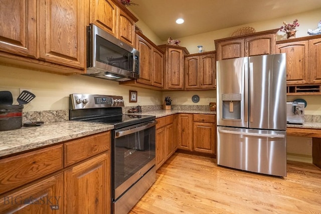 kitchen with stainless steel appliances, brown cabinetry, light wood-style flooring, and light stone counters