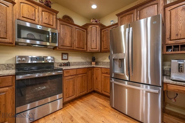 kitchen featuring light wood-style flooring, recessed lighting, stainless steel appliances, light stone countertops, and brown cabinetry