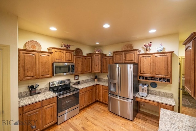 kitchen with brown cabinetry, appliances with stainless steel finishes, light stone countertops, light wood-style floors, and recessed lighting