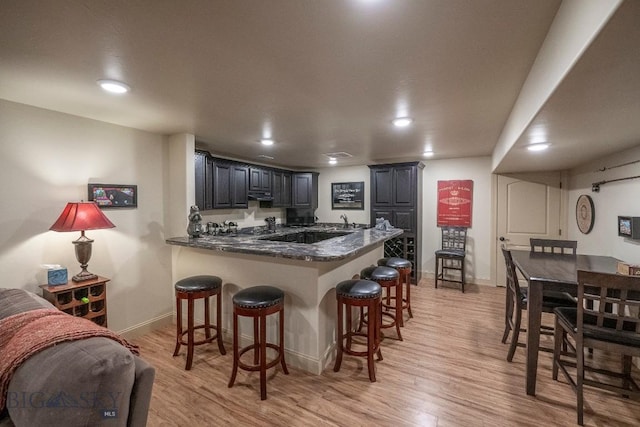 kitchen featuring a sink, light wood finished floors, a breakfast bar area, and a peninsula