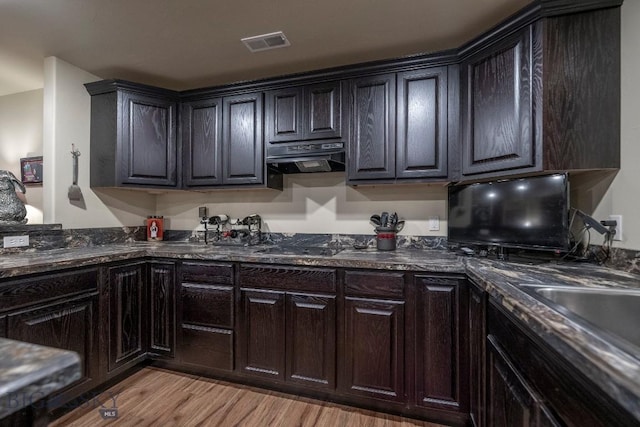 kitchen with visible vents, light wood-style flooring, dark stone countertops, dark brown cabinets, and under cabinet range hood