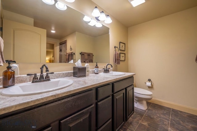 full bath featuring double vanity, a sink, toilet, and baseboards