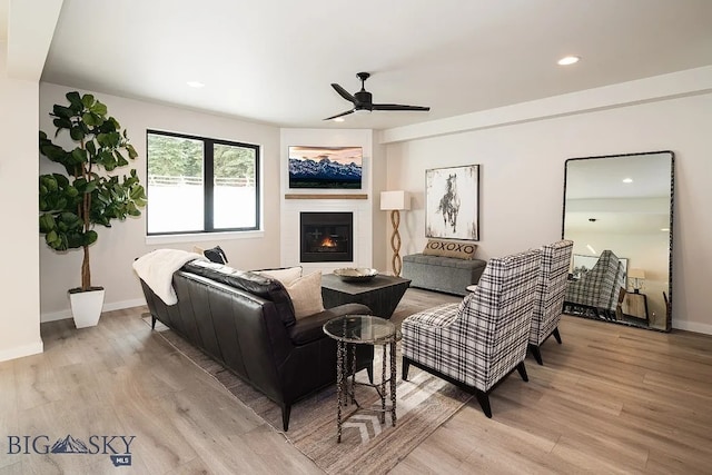 living room with light wood finished floors, a glass covered fireplace, baseboards, and ceiling fan