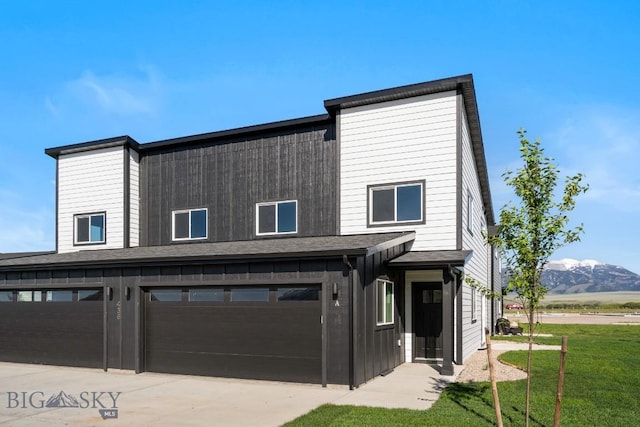 view of front facade featuring an attached garage, a mountain view, driveway, roof with shingles, and a front lawn