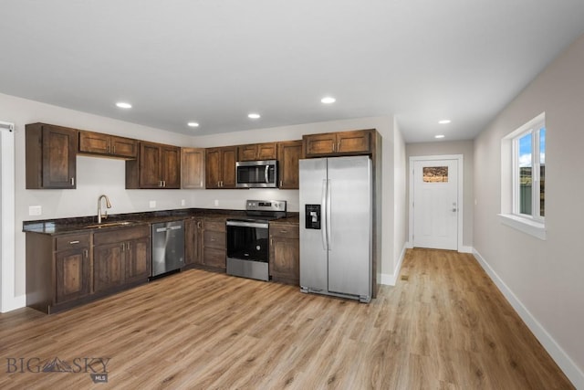 kitchen featuring stainless steel appliances, dark countertops, recessed lighting, light wood-style floors, and a sink