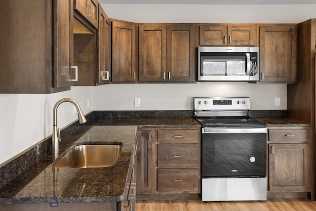 kitchen with dark stone counters, appliances with stainless steel finishes, a sink, and light wood-style floors