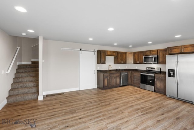 kitchen featuring stainless steel appliances, dark countertops, light wood-style flooring, and a barn door