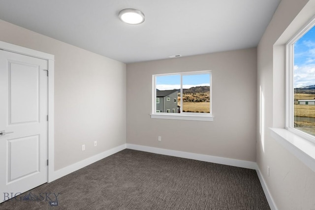 unfurnished room featuring dark carpet and baseboards