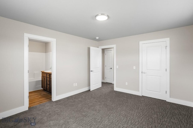 unfurnished bedroom with baseboards, dark carpet, and ensuite bathroom