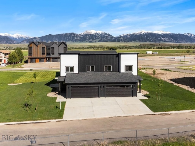 view of front of property featuring a shingled roof, concrete driveway, a mountain view, a garage, and a front lawn