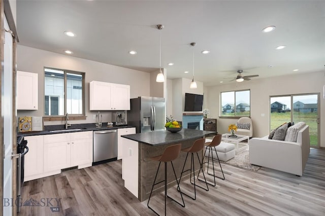 kitchen with stainless steel appliances, a sink, open floor plan, dark countertops, and a kitchen bar