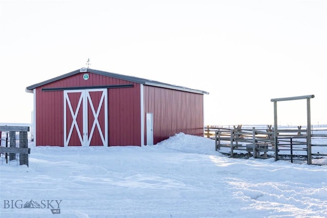 snow covered structure with an outbuilding, a barn, and fence
