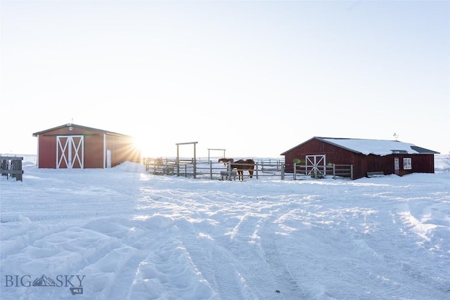 snow covered structure featuring an outdoor structure, fence, and a barn