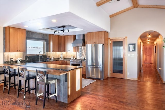 kitchen featuring dark wood-style floors, a peninsula, a sink, wall chimney range hood, and high quality appliances