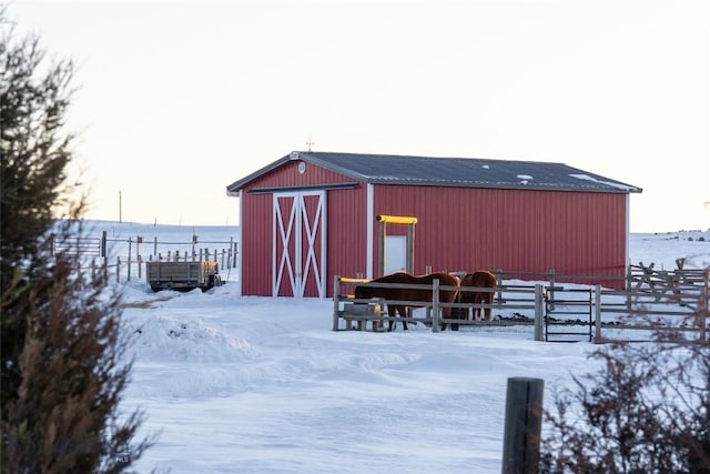 snow covered structure featuring an outbuilding, fence, and a barn