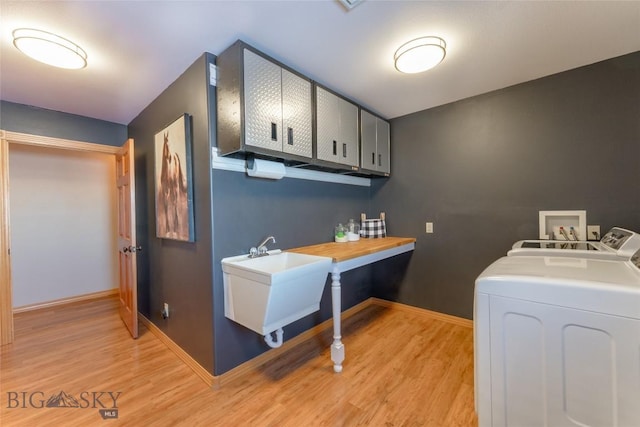 clothes washing area featuring independent washer and dryer, light wood-style flooring, a sink, cabinet space, and baseboards