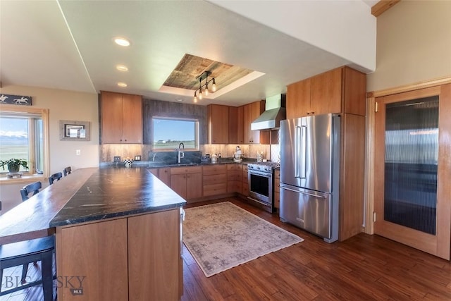 42 Jim Parrent Ln, Big Timber, MT 59011 - kitchen featuring high end appliances, a raised ceiling, dark countertops, wall chimney exhaust hood, and a sink