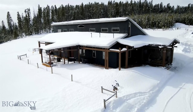 snow covered house with a garage and a forest view